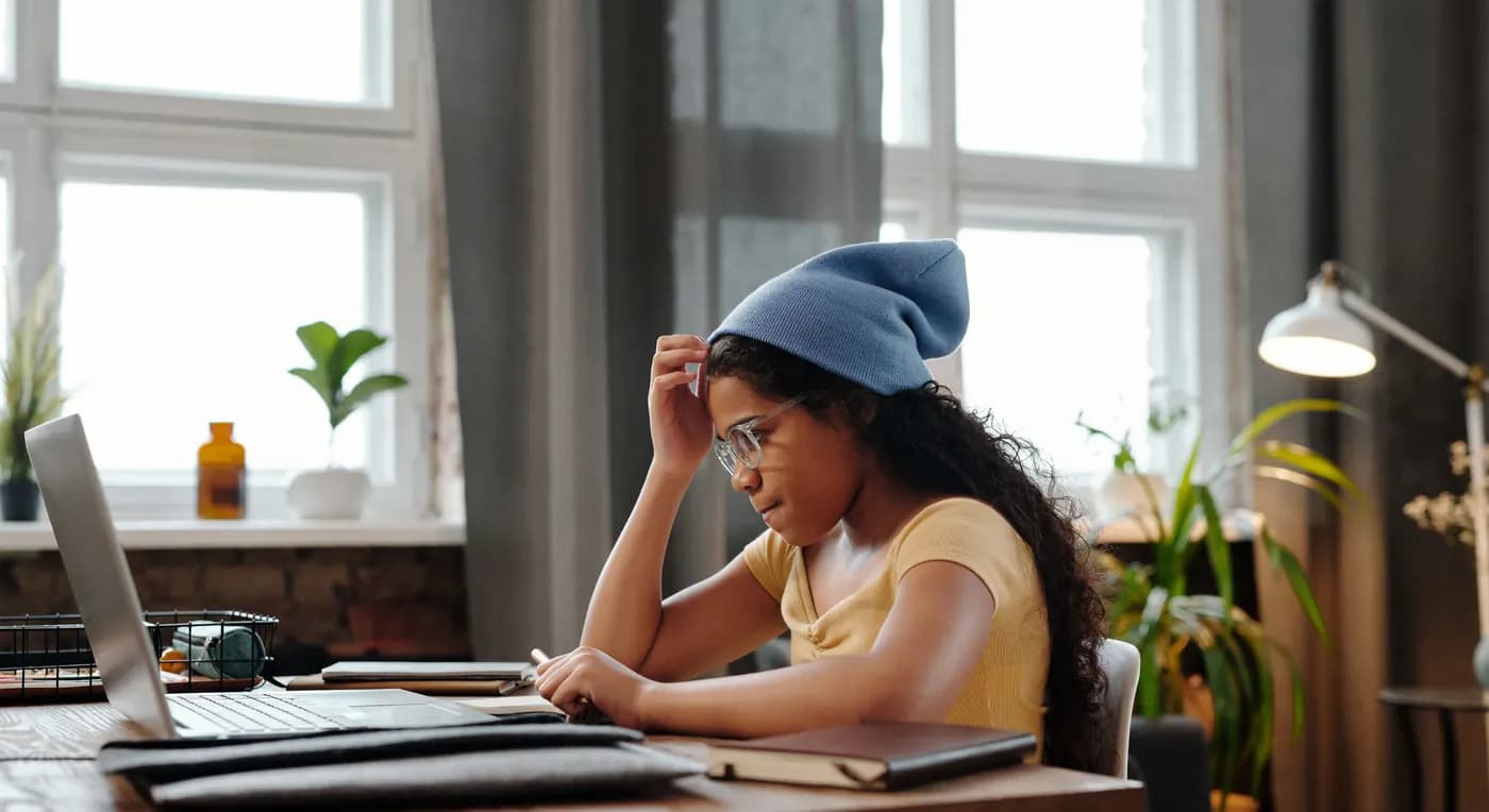 A student working on a laptop at a desk by the window.