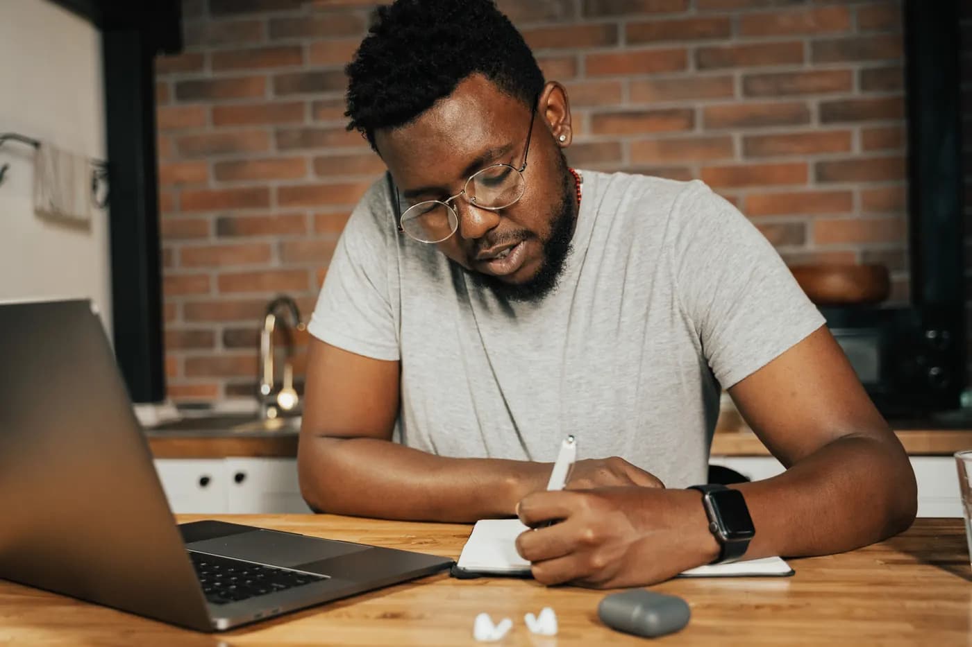 A learner taking notes beside a laptop at home.